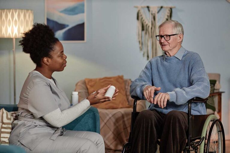 Two older adults sitting with a caregiver discussing medications in a bright, comfortable common area.